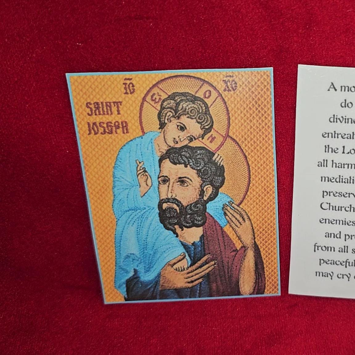 Saint Joseph holding baby Jesus against yellow-orange textured background with halo and religious iconography