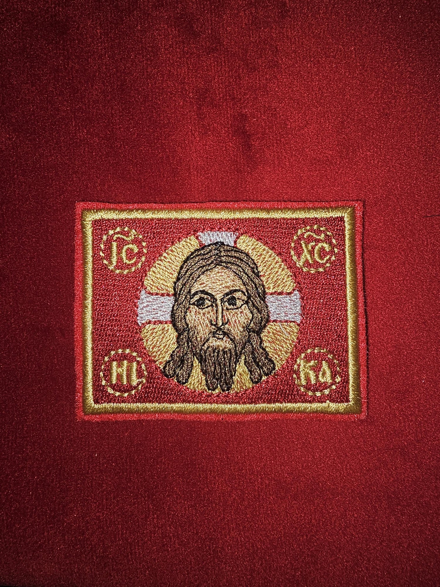 Embroidered religious icon of Jesus with halo on red textured background